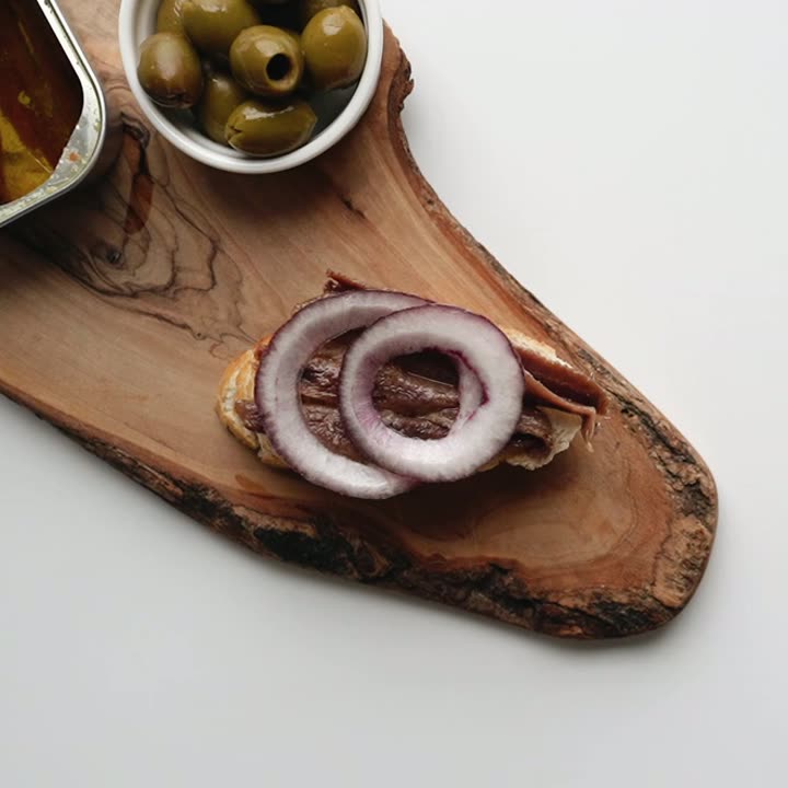 Boquerones en vinagre con cebolla sobre pan, en tabla de olivo
